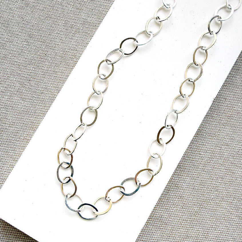 Chunky silver chain necklace on a white card with a gray background