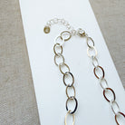 Chunky silver chain necklace on a white and beige fabric background