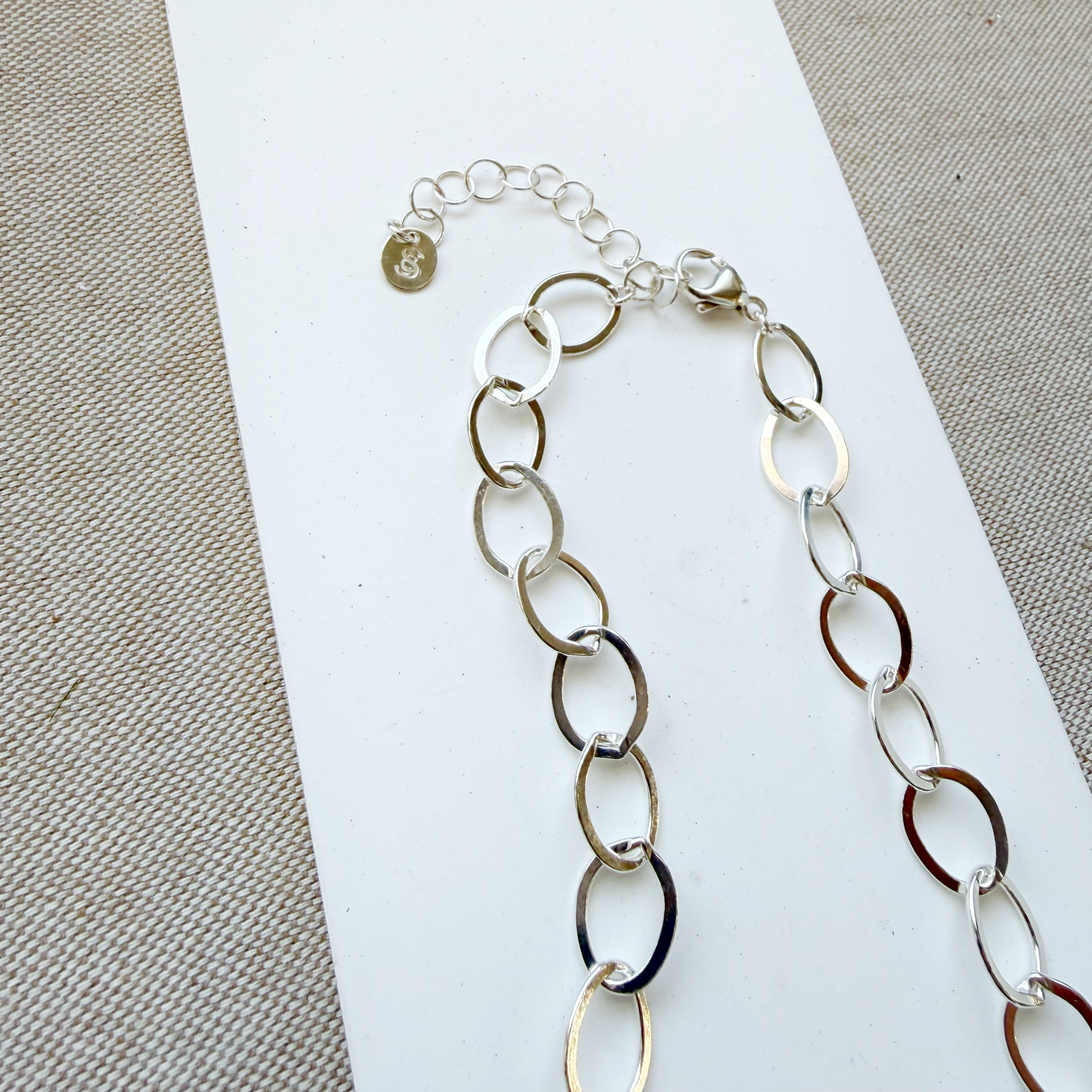 Chunky silver chain necklace on a white and beige fabric background