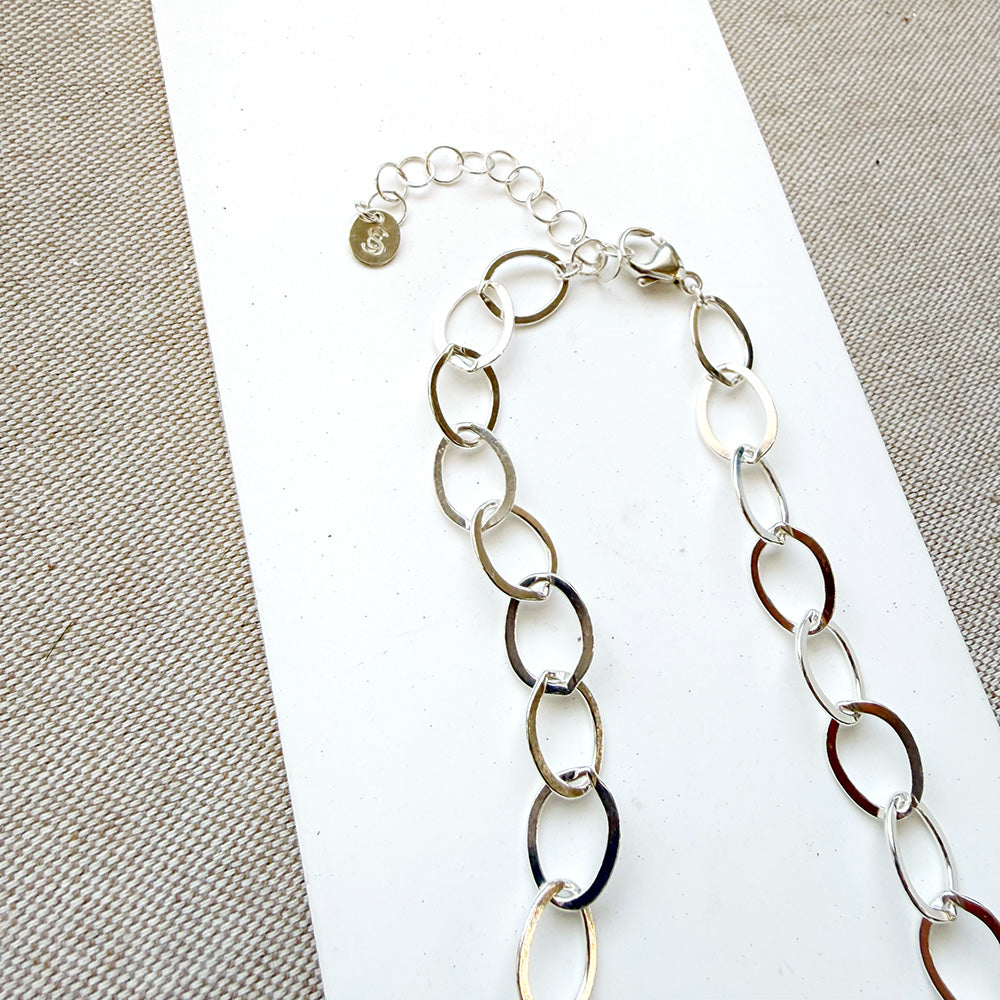 Chunky silver chain necklace on a white card with a gray background