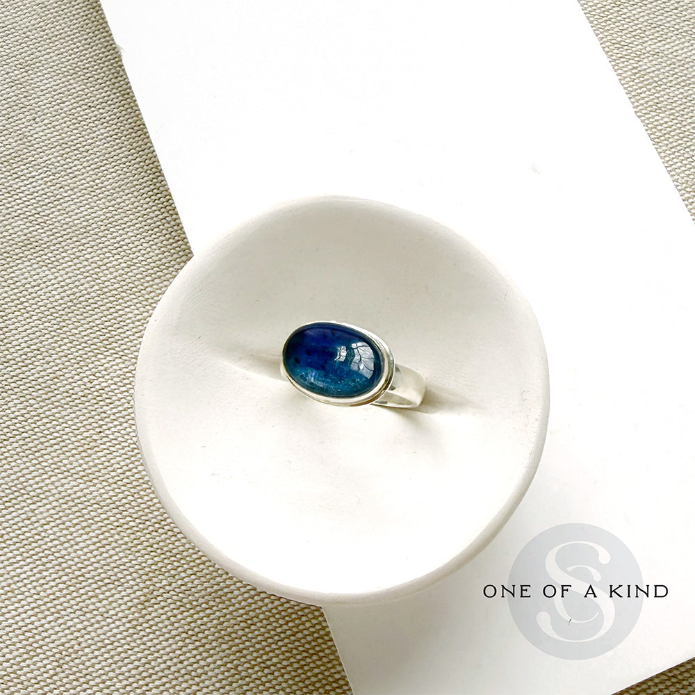 Oval shaped smooth blue kyanite mixed metal ring in a white dish