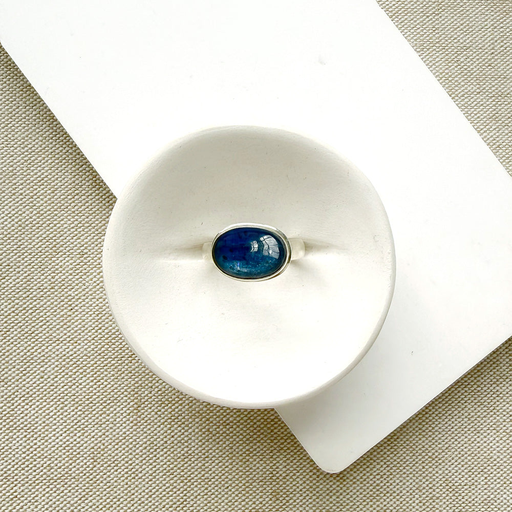 Oval shaped smooth blue kyanite mixed metal ring in a white dish