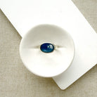 Oval shaped smooth blue kyanite mixed metal ring in a white dish