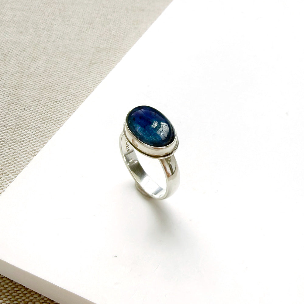Oval shaped smooth blue kyanite mixed metal ring on a white dish