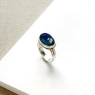 Oval shaped smooth blue kyanite mixed metal ring on a white dish
