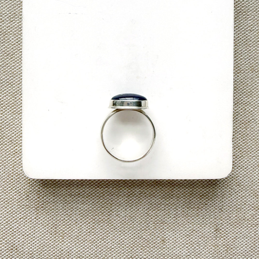 Oval shaped smooth blue kyanite mixed metal ring on a white dish