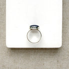 Oval shaped smooth blue kyanite mixed metal ring on a white dish