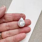 Hand holding a tear drop shaped pearl charm