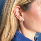 Close-up of a person wearing a gold hammered disc earring against a blue background.