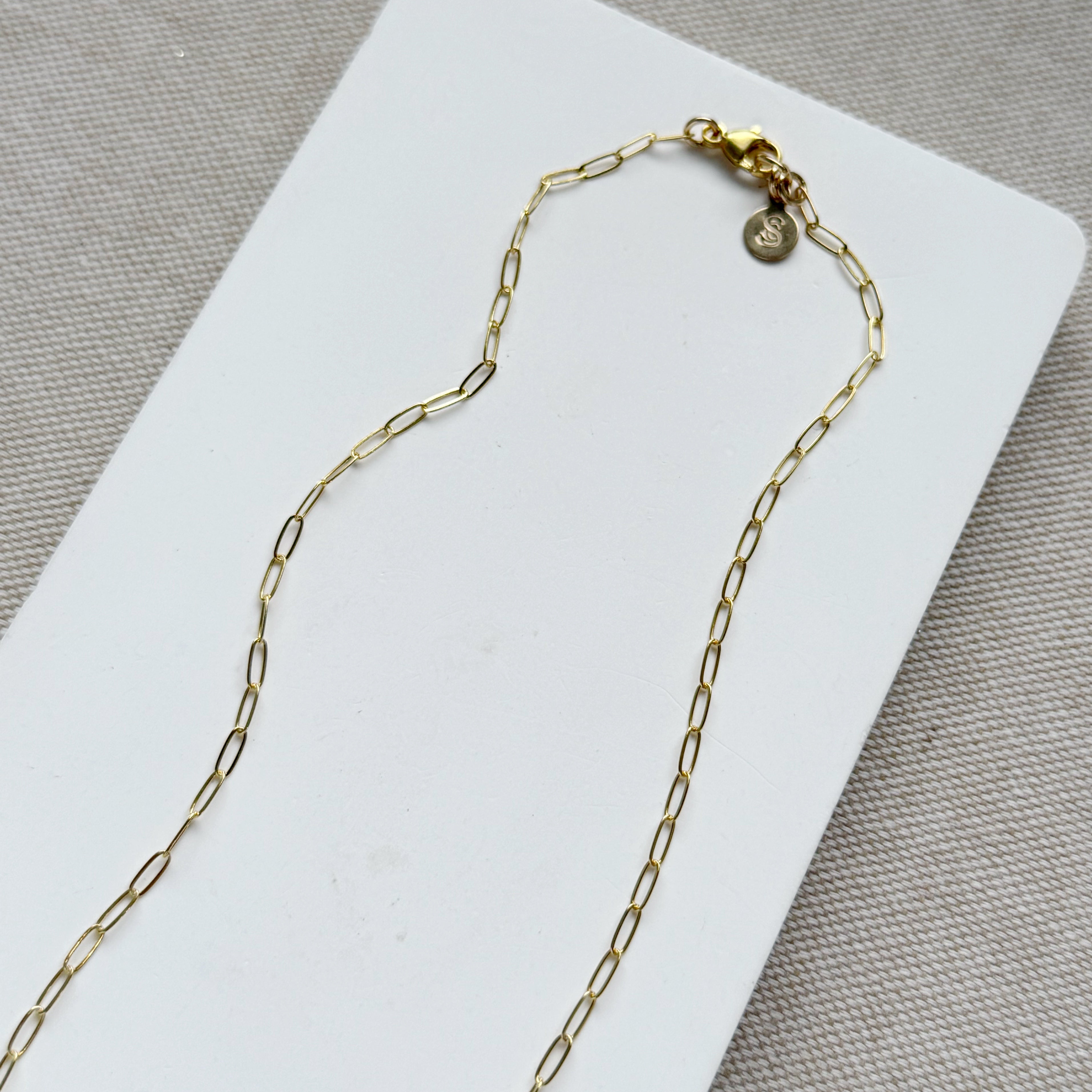Clasp detail of gold and baroque pearl necklace on a white tray