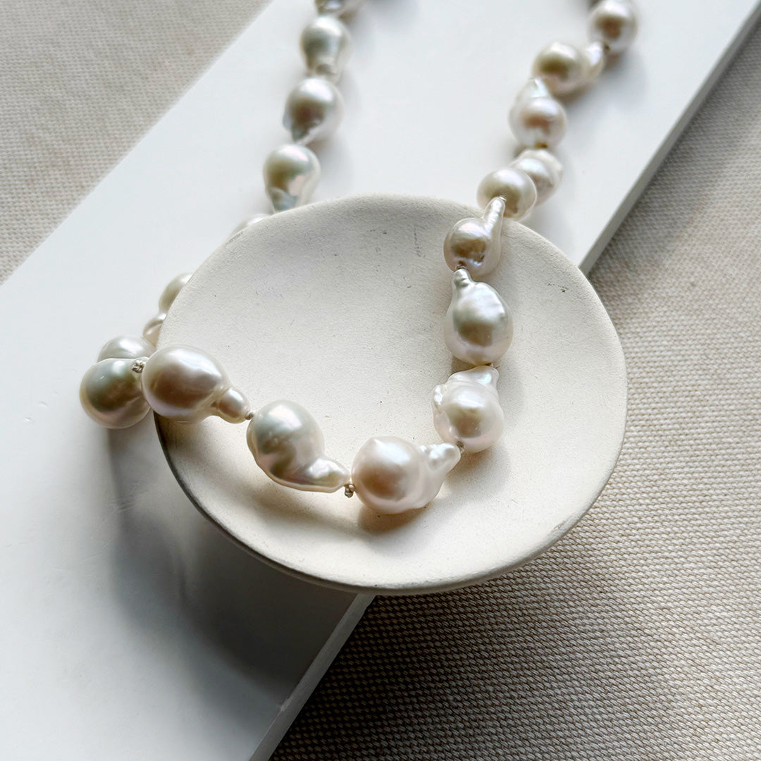 Baroque pearl necklace draped over a white dish on a neutral background