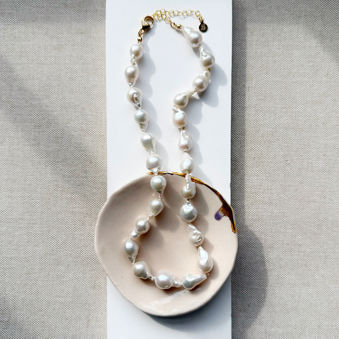 Baroque pearl necklace on a decorative plate with a neutral background