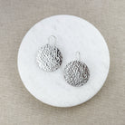 Pair of large round silver earrings on a round marble coaster