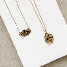 Two gold necklaces with butterfly and beetle pendants on a white surface
