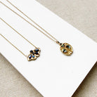 Two gold necklaces with butterfly and beetle pendants on a white surface
