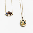 Two gold necklaces with butterfly and beetle pendants on a white surface