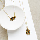 Two gold necklaces with butterfly and beetle pendants on a white surface