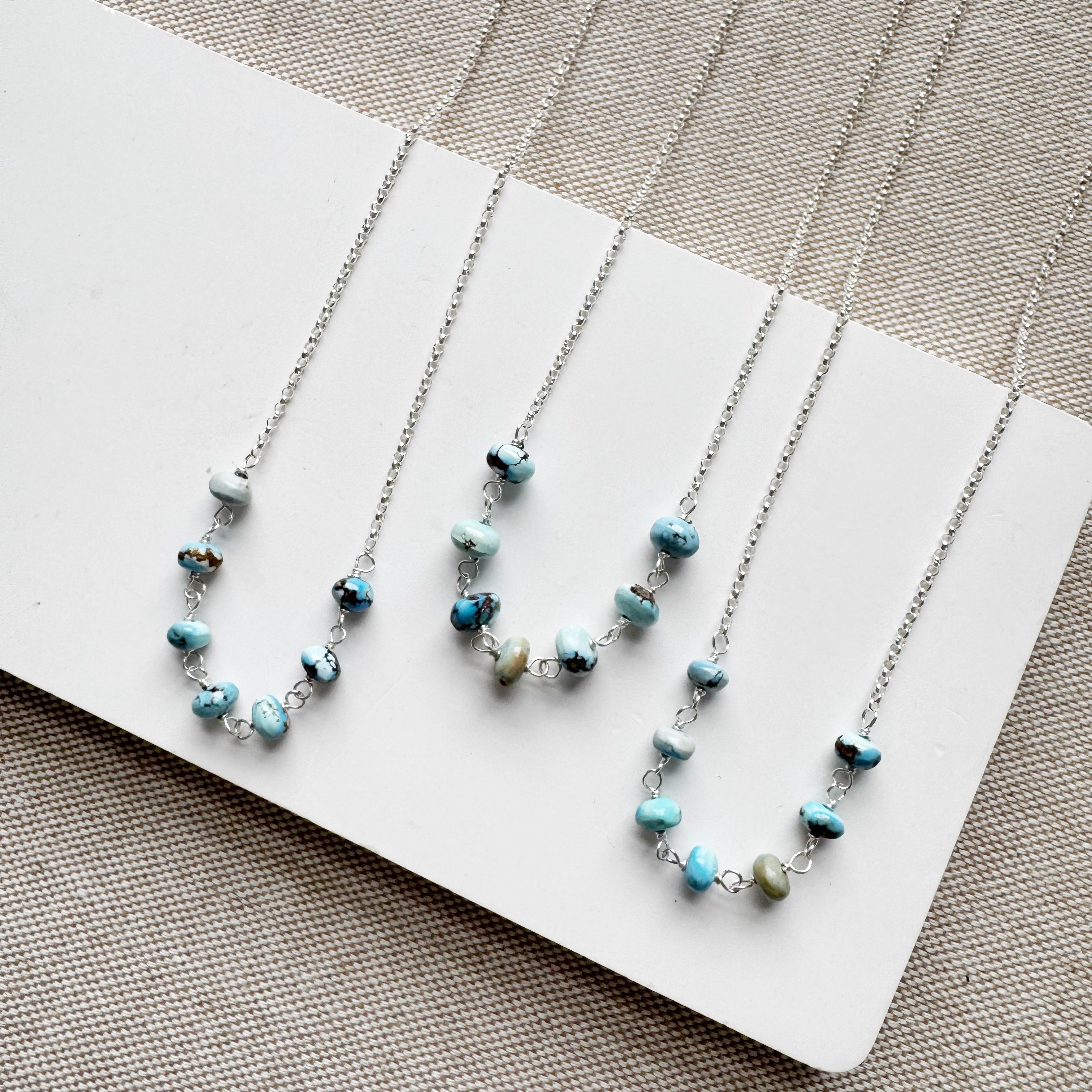 Silver chain necklaces in Golden Hill turquoise beads on a white card against a beige background
