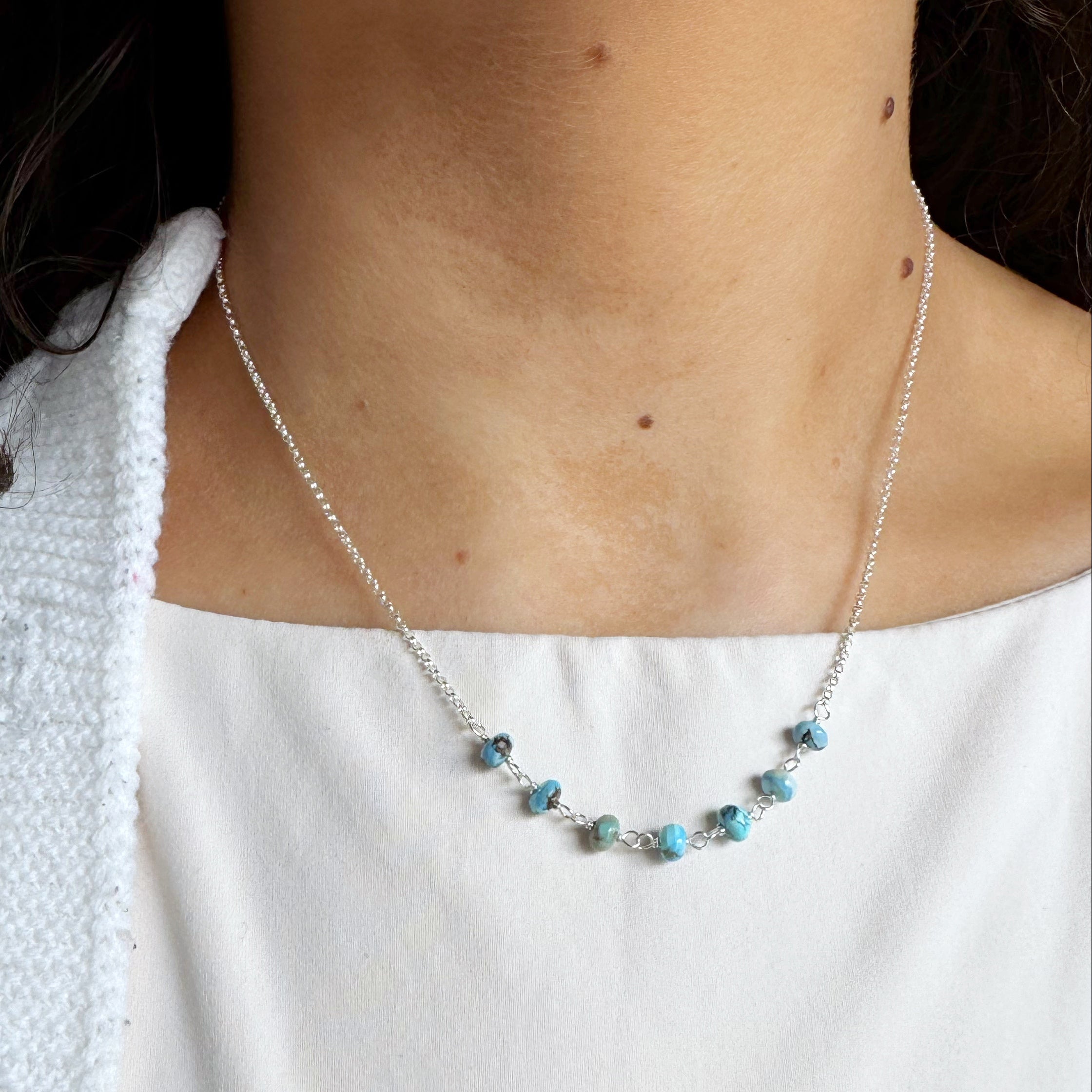 Silver necklace with small Golden Hill Turquoise beads worn by a person against a white background