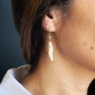 Woman wearing stick pearl earring on a blue background