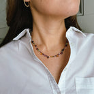 Person wearing a colorful gemstone necklace with a white shirt.