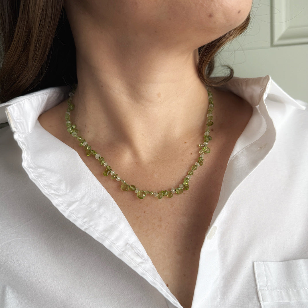 Person wearing a gemstone necklace in shades of green with a white shirt