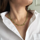 Person wearing a gemstone necklace in shades of green with a white shirt