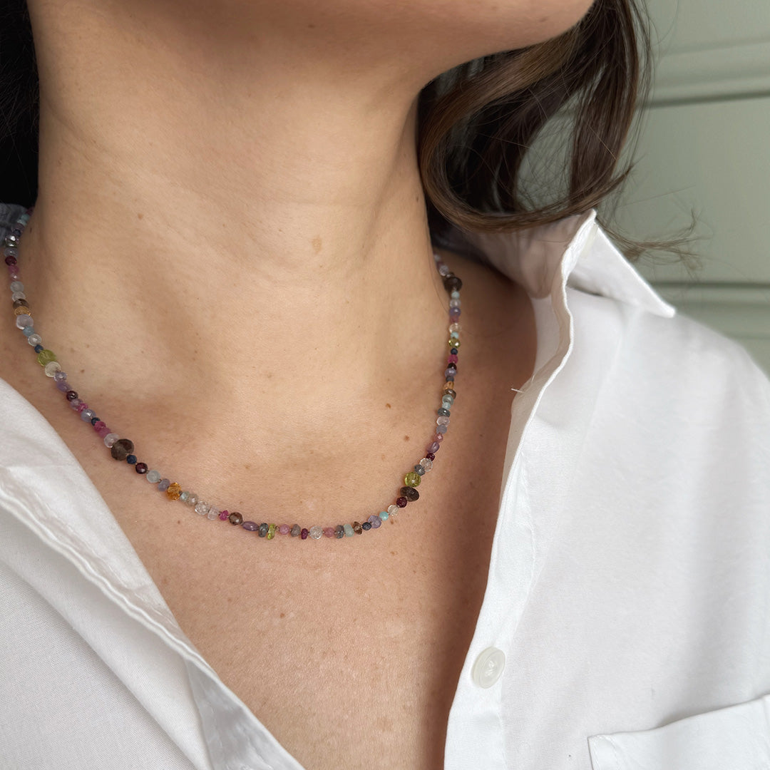 Multicolored gemstone necklace worn by a person with a white shirt.