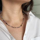 Multicolored gemstone necklace worn by a person with a white shirt.