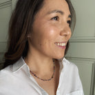 Woman wearing a white shirt and a multicolored gemstone necklace with a neutral background