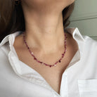 Gemstone necklace in shades of red worn by a person in a white shirt.