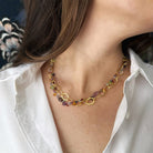 Necklace with multicolored gemstones and gold chain worn by a person in a white shirt.