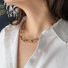 Close-up of a person wearing a gold chain necklace with colorful gemstones.