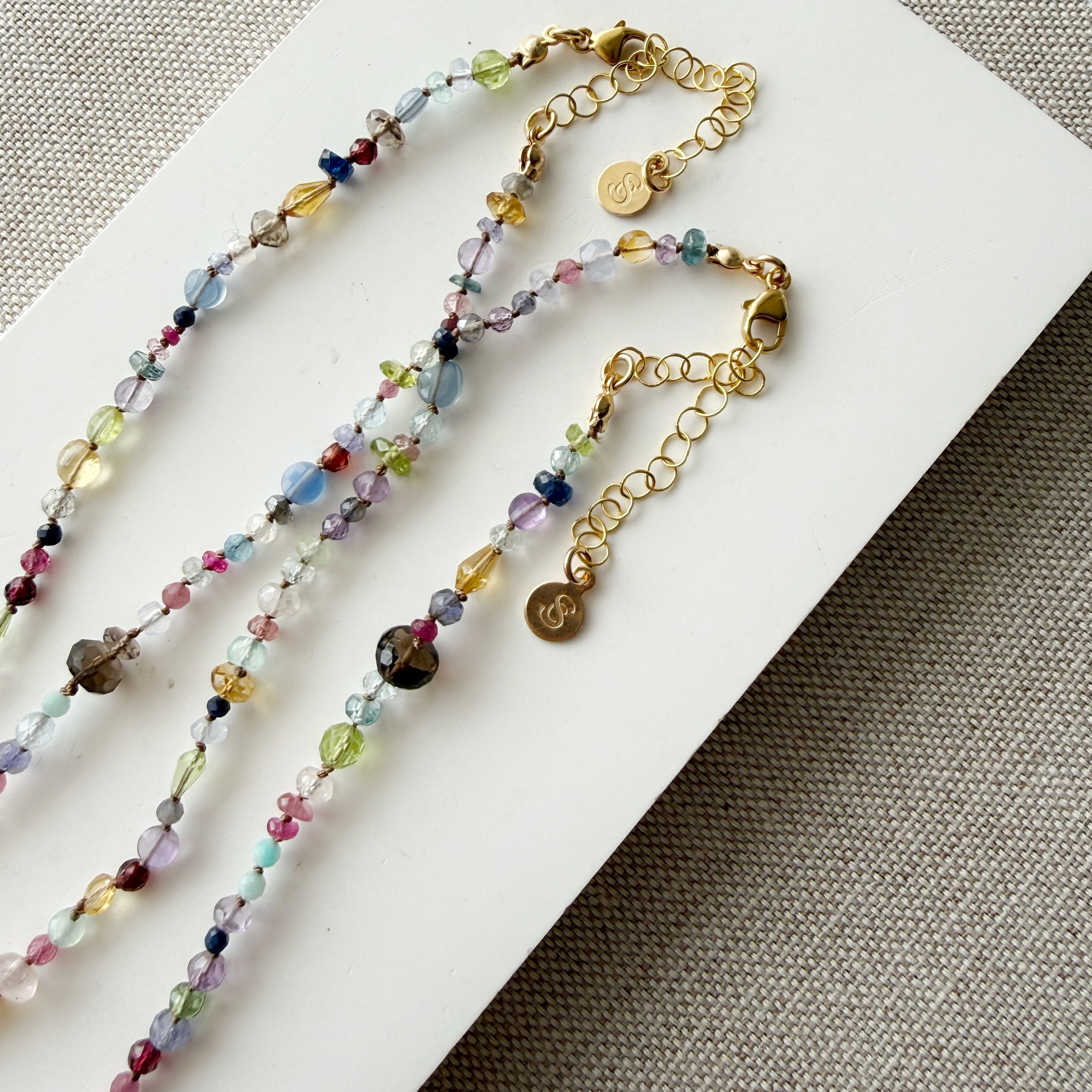 Clasp and extender of a multicolored gemstone necklace on a textured beige background