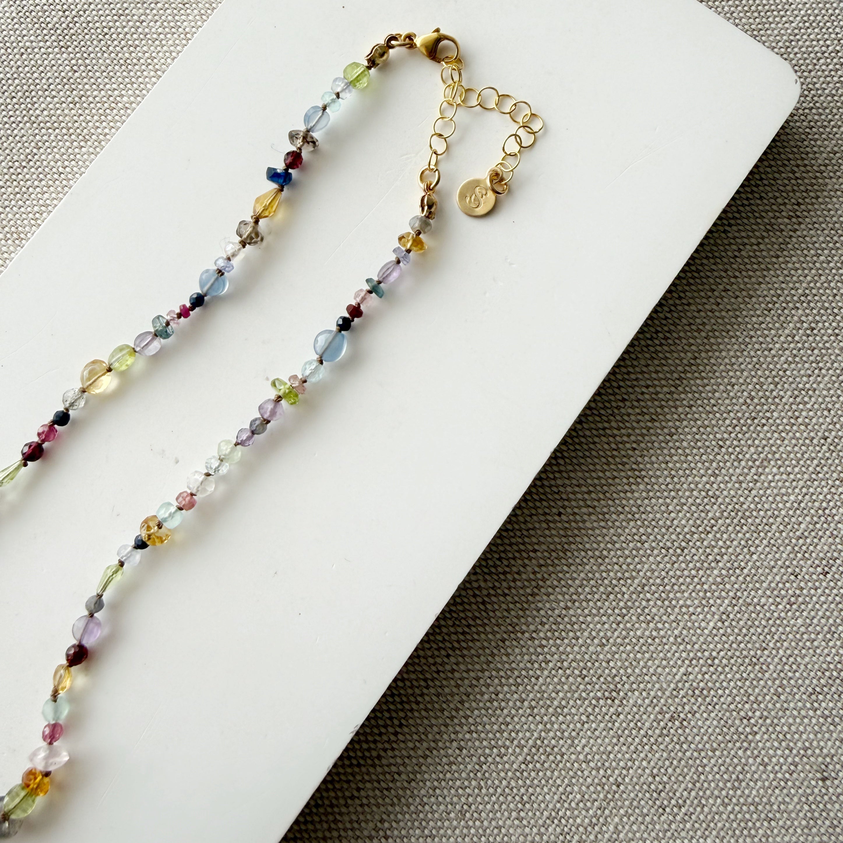 Clasp and extender of a multicolored gemstone necklace on a white card with a textured brown background