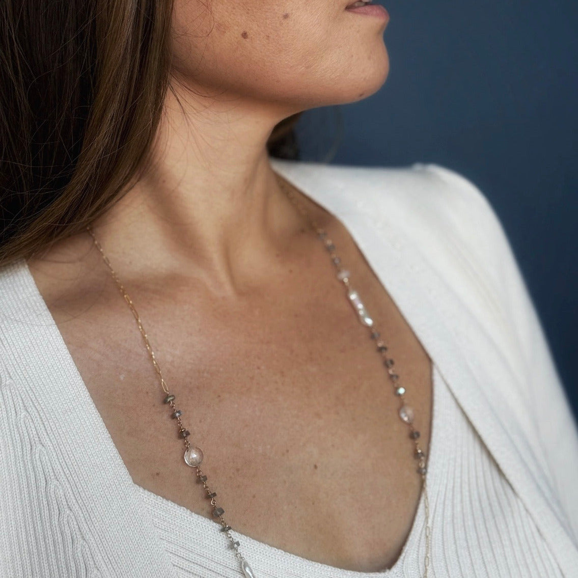 Woman wearing long necklace with labradorite gems and stick pearls on a blue background
