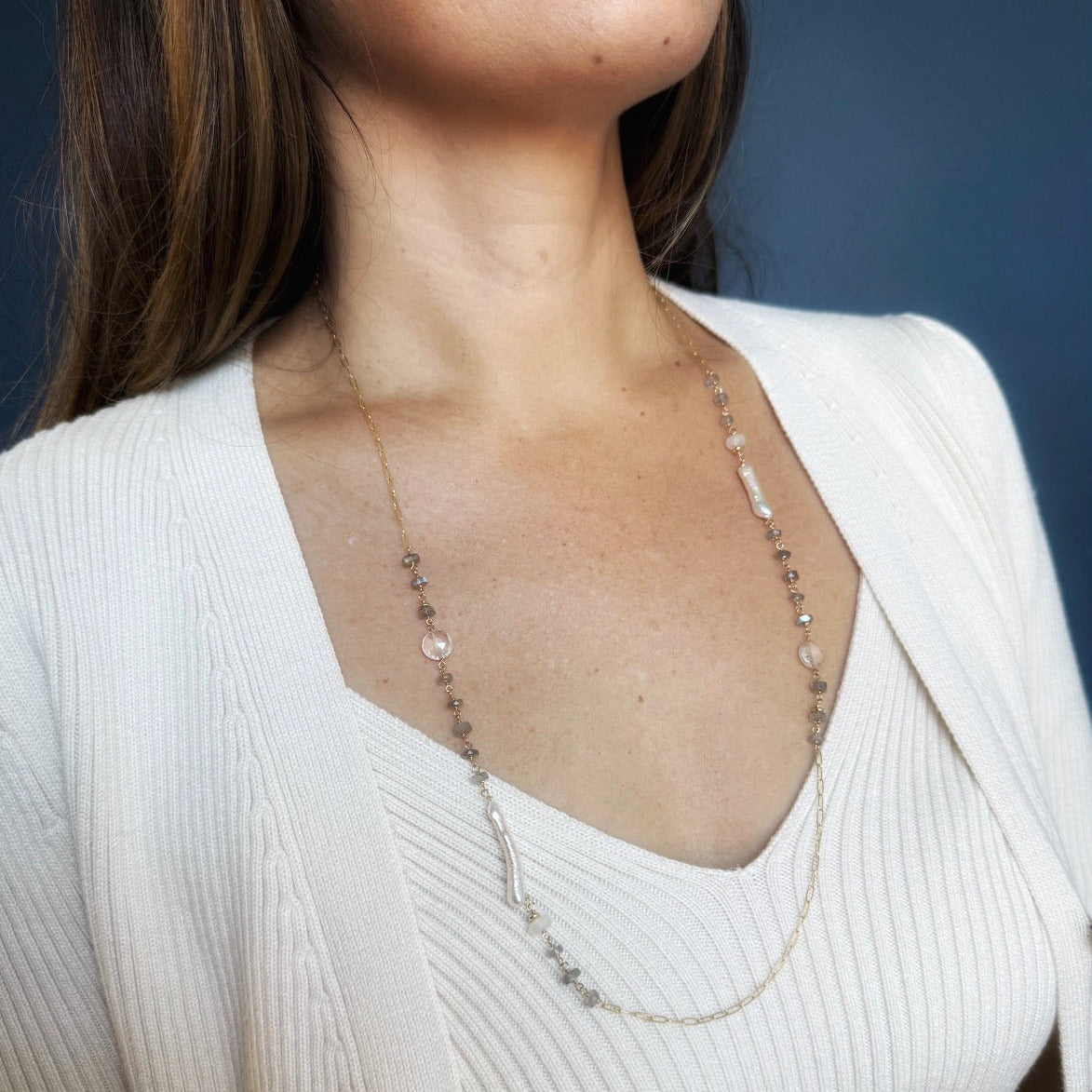 Woman wearing long necklace with labradorite gems and stick pearls on a blue background