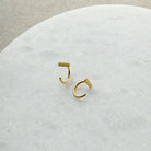 Tiny gold bar huggie style earrings on a white marble background