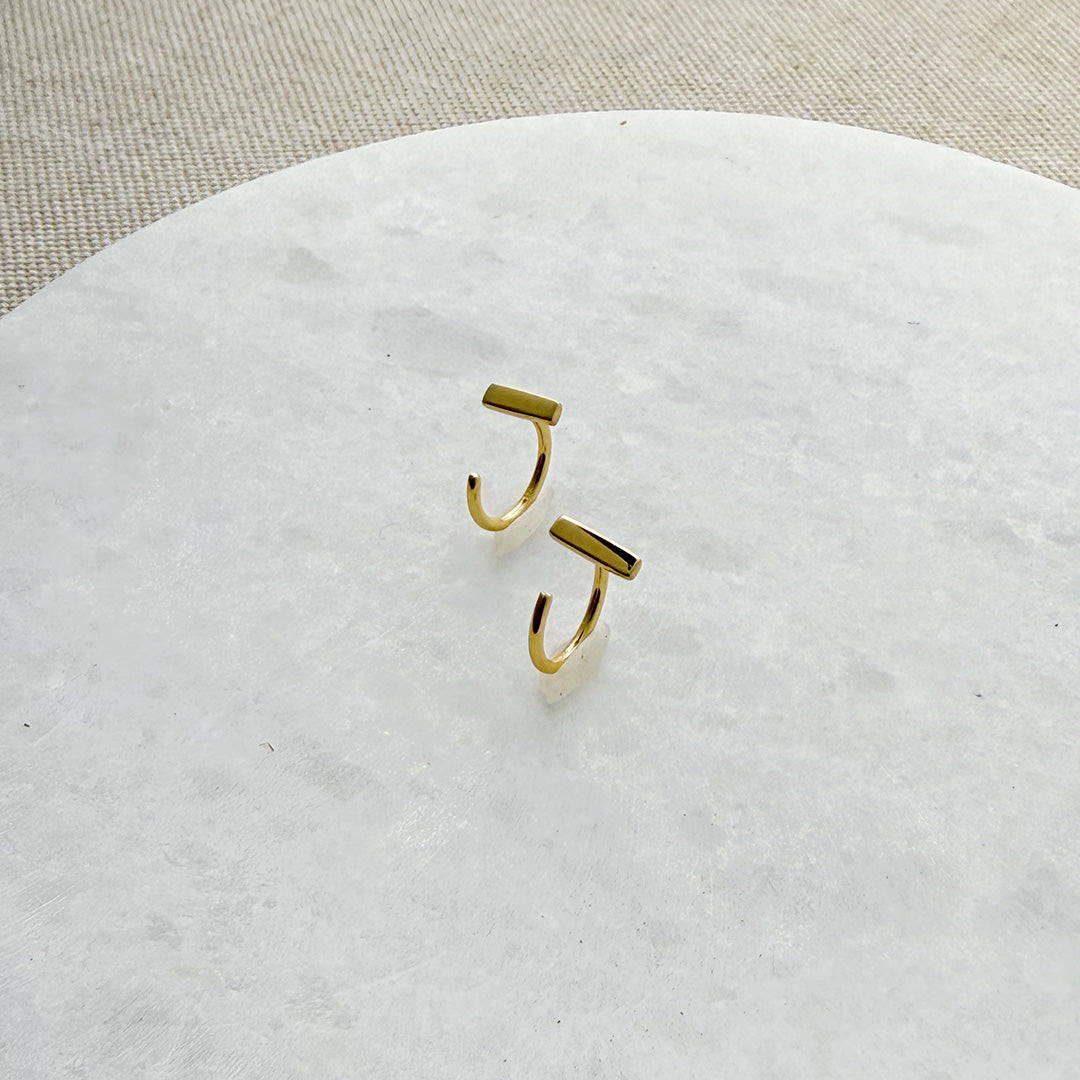 Tiny gold bar huggie style earrings on a white marble background