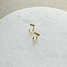 Tiny gold bar huggie style earrings on a white marble background