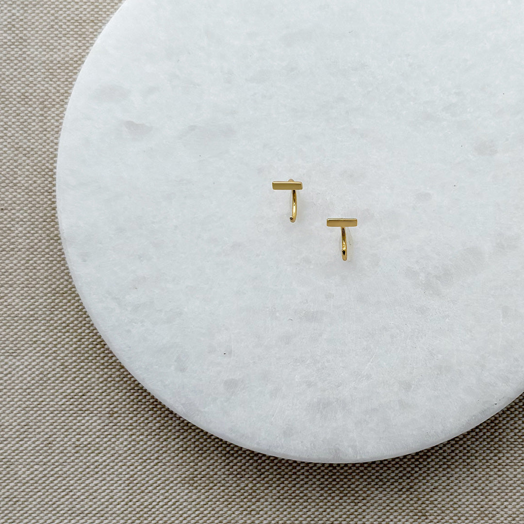 Tiny gold bar huggie style earrings on a white marble background