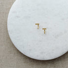 Tiny gold bar huggie style earrings on a white marble background