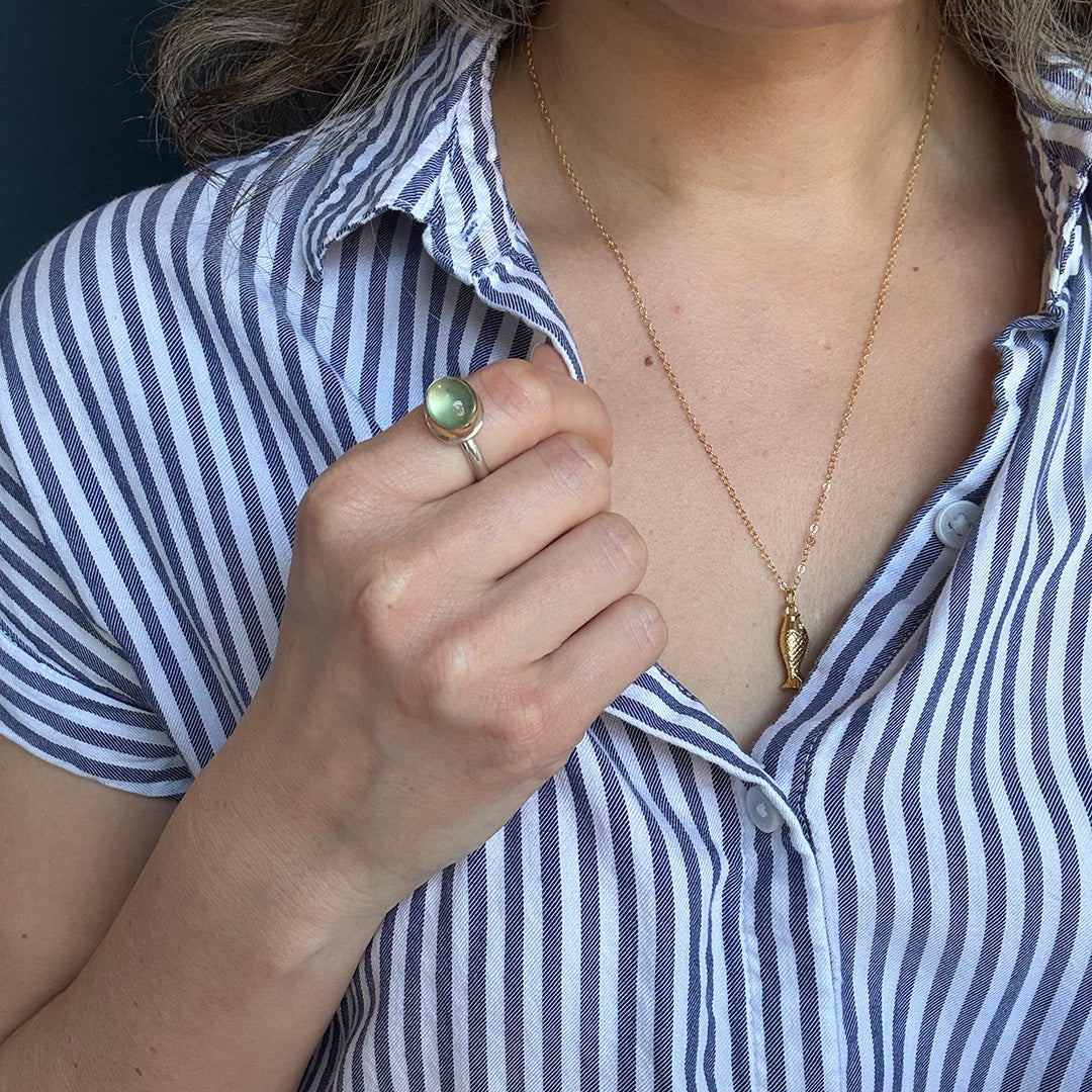 Person wearing a gold necklace and wearing a green prehnite gemstone ring.