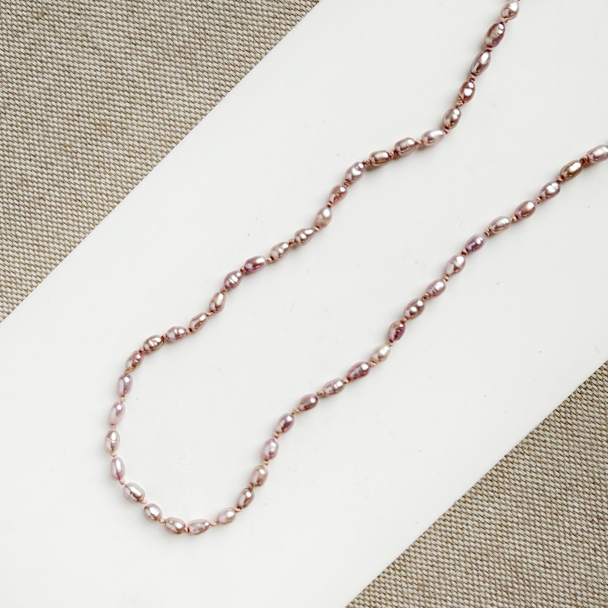 Detail of knotted necklace with tiny pink pearls on a white card