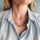 Necklace with multicolored gemstones worn by a person in a white top against a blurred background