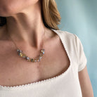 Necklace with multicolored gemstones worn by a person in a white top against a blurred background