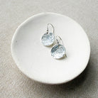 Silver disc earrings on a round white stone surface