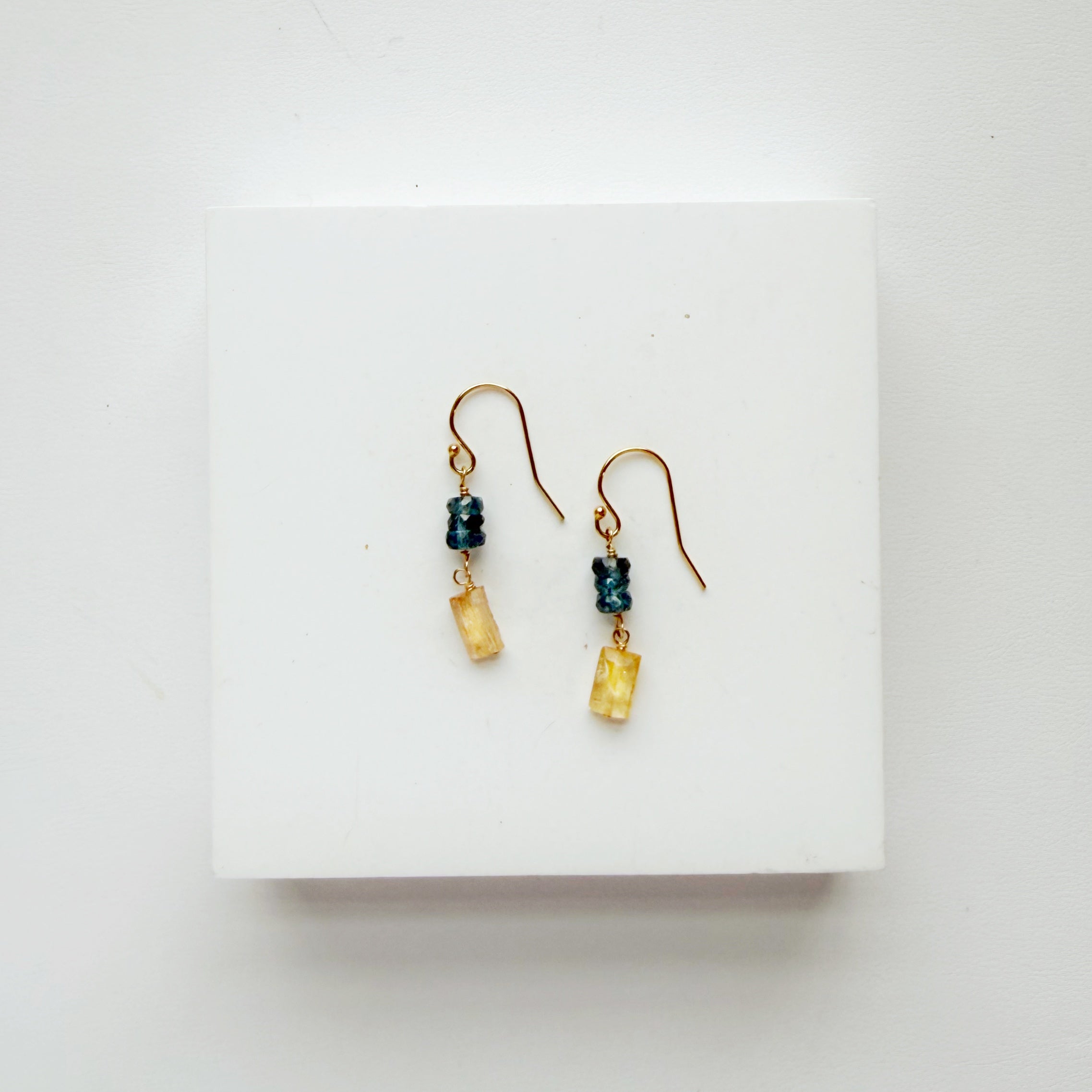 Pair of gold earrings with blue and yellow gems on a white background