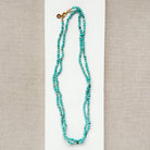 Long turquoise beaded necklace on a beige background