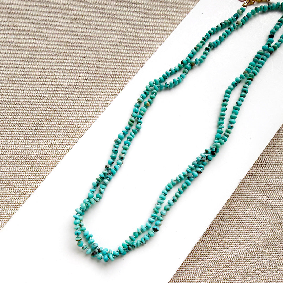 Turquoise beaded necklace on a white and beige fabric background